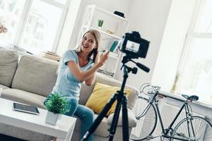 mooi jong vrouw glimlachen en toepassen schoonheid producten Aan haar haar- terwijl maken sociaal media video Bij huis foto