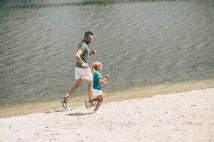 genieten van jogging Aan vers lucht. top visie van vrolijk vader en dochter in sport- kleren jogging Bij de oever van de rivier samen foto