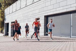 vol lengte van jong mensen in sport- kleding jogging terwijl oefenen Aan de trottoir buitenshuis foto