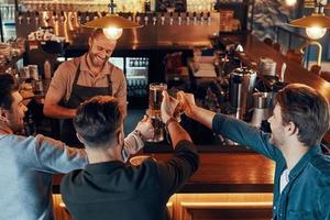 top visie van zorgeloos jong mannen in gewoontjes kleding drinken bier terwijl zittend in de kroeg foto