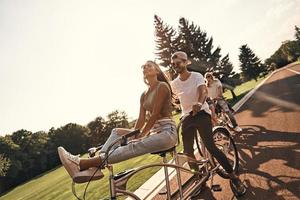 genieten van vrijheid. groep van gelukkig jong mensen in gewoontjes slijtage glimlachen terwijl wielersport samen buitenshuis foto