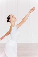 genade in elke Actie. mooi jong ballerina in wit tutu dansen in ballet studio foto