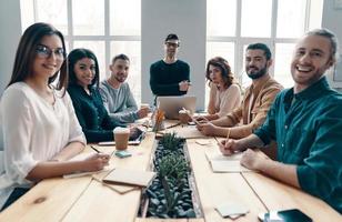 droom team. groep van jong modern mensen in slim gewoontjes op zoek Bij camera en glimlachen terwijl werken in de creatief kantoor foto