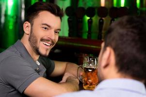 uitgeven tijd in bar. twee vrolijk mannen pratend naar elk terwijl drinken bier in bar foto