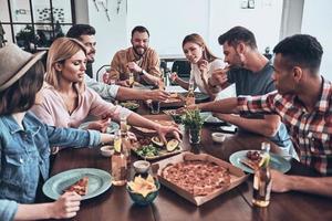 avondeten is Aan de tafel. groep van jong mensen in gewoontjes slijtage aan het eten en glimlachen terwijl hebben een avondeten partij foto