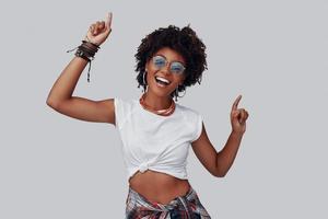 aantrekkelijk jong Afrikaanse vrouw op zoek Bij camera en glimlachen terwijl staand tegen grijs achtergrond foto
