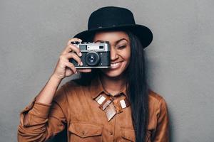 zeggen kaas mooi vrolijk jong Afrikaanse vrouw Holding retro gestileerd camera en scherpstellen Aan u met glimlach terwijl staand tegen grijs achtergrond foto