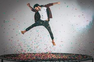 ontketend plezier. in de lucht schot van knap jong Mens jumping Aan trampoline met confetti allemaal in de omgeving van hem foto