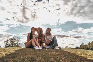 eenvoudig gelukkig. jong modern paar zittend Aan de gras met hun hond terwijl uitgeven vrij tijd in de park foto