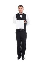 zelfverzekerd bediende. vol lengte van zelfverzekerd mannetje ober draag- handdoek in hand- en glimlachen terwijl staand tegen wit achtergrond foto