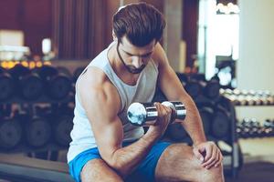 voelen de brandwond in biceps. zelfverzekerd jong knap Mens in sportkleding oefenen met halter Bij Sportschool foto