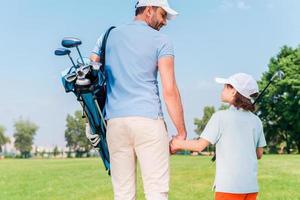 het was een Super goed spel achterzijde visie van jong Mens en zijn zoon Holding handen en op zoek Bij elk andere terwijl wandelen Aan de golf Cursus foto