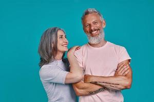 mooi senior paar op zoek Bij camera en glimlachen terwijl staand samen tegen blauw achtergrond foto