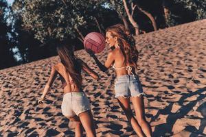 gevoel speels. twee aantrekkelijk jong Dames in shorts en badmode glimlachen terwijl rennen Aan de strand foto