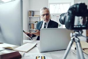 senior Mens in elegant bedrijf pak gebruik makend van modern technologieën terwijl maken sociaal media video foto