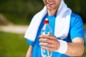 krijgen verfrist detailopname van jong Mens uitrekken uit een fles met water en glimlachen terwijl staand buitenshuis foto