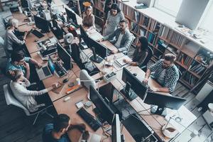 zelfverzekerd bedrijf experts een werk. top visie van groep van jong bedrijf mensen in slim gewoontjes slijtage werken samen terwijl zittend Bij de groot kantoor bureau foto