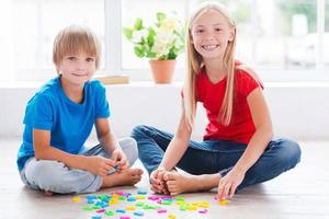 spelen en aan het studeren. twee schattig weinig kinderen spelen met plastic kleurrijk brieven terwijl zittend Aan de hardhout verdieping foto