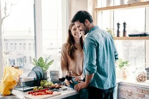 hij zullen nooit laat haar Gaan. mooi jong paar Koken avondeten en drinken wijn terwijl staand in de keuken Bij huis foto