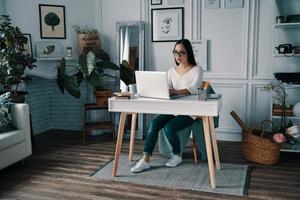 krijgen dingen gedaan. mooi jong vrouw werken gebruik makend van computer terwijl zittend in huis kantoor foto