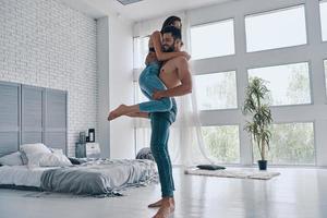 gevoel speels samen. vol lengte van mooi jong paar omarmen en glimlachen terwijl dansen in de slaapkamer foto