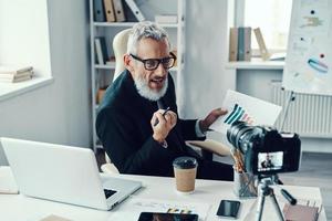 zelfverzekerd volwassen Mens in elegant pak tonen tabel en sharing bedrijf ervaring terwijl maken sociaal media video foto