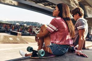 plaats ze liefde. mooi jong vrouw zittend Aan de skateboard en op zoek weg terwijl uitgeven tijd met haar vriend buitenshuis foto