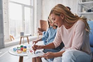 favoriete werkzaamheid. moeder en dochter schilderij met vingers en glimlachen terwijl uitgeven tijd Bij huis foto