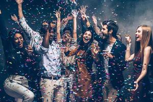 hebben pret samen. groep van mooi jong mensen het werpen kleurrijk confetti en op zoek gelukkig foto