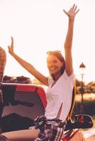 in zoeken van avonturen. mooi jong vrouw houden armen verheven en glimlachen terwijl genieten van weg reis in oppakken vrachtauto foto