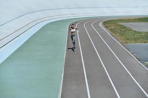 haar het beste snelheid. vol lengte top visie van jong vrouw in sport- kleding jogging terwijl oefenen buitenshuis foto