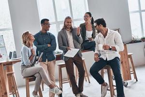 gebruikt naar succes. groep van jong modern mensen in slim gewoontjes slijtage glimlachen en bespreken iets terwijl werken in de creatief kantoor foto