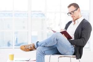 knap boekenwurm. attent jong Mens in overhemd zittend Aan de stoel en lezing een boek foto