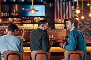 achterzijde visie van gelukkig jong mannen in gewoontjes kleding genieten van bier foto