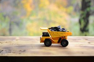 een klein geel speelgoed- vrachtauto is geladen met zonnebloem zaden. een auto Aan een houten oppervlakte tegen een achtergrond van herfst Woud. extractie en vervoer van zonnebloem zaden foto
