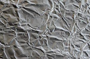 dun gerimpeld vel van verpletterd blik aluminium zilver folie achtergrond met glimmend verfrommeld oppervlakte voor structuur foto