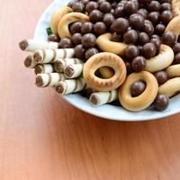 krokant buisjes, chocola smelten ballen en bagels liggen in een wit bord Aan een houten tafel. mengen van divers snoepgoed foto