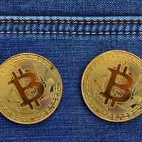 twee gouden bitcoins is leugens Aan een blauw jeans kleding stof. nieuw virtueel geld. nieuw crypto valuta in de het formulier van de munten foto