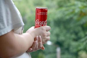 Charkov. Oekraïne - mei 2, 2019 Kaukasisch vrouw houdt rood Coca Cola blik kan met groen tuin achtergrond foto