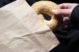 een man's hand- is Holding een bagel uit van een bruin papier tas. foto