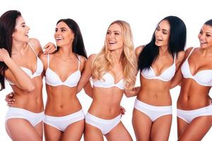 genieten van hun perfectie. groep van vijf mooi Dames in lingerie omarmen en op zoek Bij elk andere met glimlacht terwijl staand tegen wit achtergrond foto