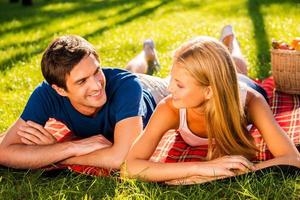 genieten van hun perfect datum samen. gelukkig jong liefhebbend paar ontspannende in park samen terwijl aan het liegen Aan picknick deken en op zoek Bij elk andere foto