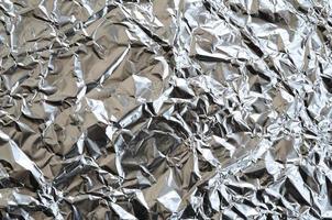 dun gerimpeld vel van verpletterd blik aluminium zilver folie achtergrond met glimmend verfrommeld oppervlakte voor structuur foto