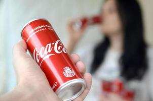 Charkov. Oekraïne - mei 2, 2019 brunette vrouw drankjes Coca Cola drinken in garage interieur en mannetje hand- presenteert een cola kan in focus foto