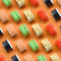 verschillend types van Aziatisch sushi broodjes Aan oranje achtergrond. minimalisme top visie vlak leggen patroon met Japans voedsel foto