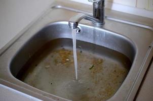 roestvrij staal wastafel plug gat dichtbij omhoog vol van water en deeltjes van voedsel foto