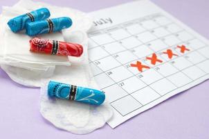 menstruatie- stootkussens en tampons Aan menstruatie periode kalender met rood kruis merken leugens Aan lila achtergrond foto