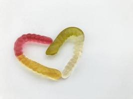 marmelade wormen. gelatineachtig wormen, veelkleurig met elkaar verweven in de vorm van een hart. geel rood en groen Wit worm Aan een wit matte achtergrond. heerlijk en smakelijk toetje foto