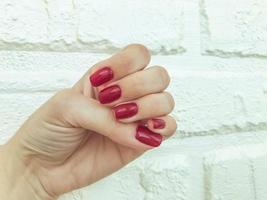 helder, rood, glanzend manicure Aan een wit matte achtergrond. steen muur van gips voor schoten van schoonheid Diensten van meesters. muur van schoonheid salon. rood nagels voor mode meisjes foto