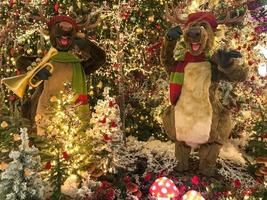 Kerstmis vooravond. Daar zijn hoog speelgoed- hert in de winkelcentrum. hert Speel muziek- Aan de saxofoon. vermaak voor bezoekers naar de boodschappen doen centrum. speelgoed voor kinderen foto